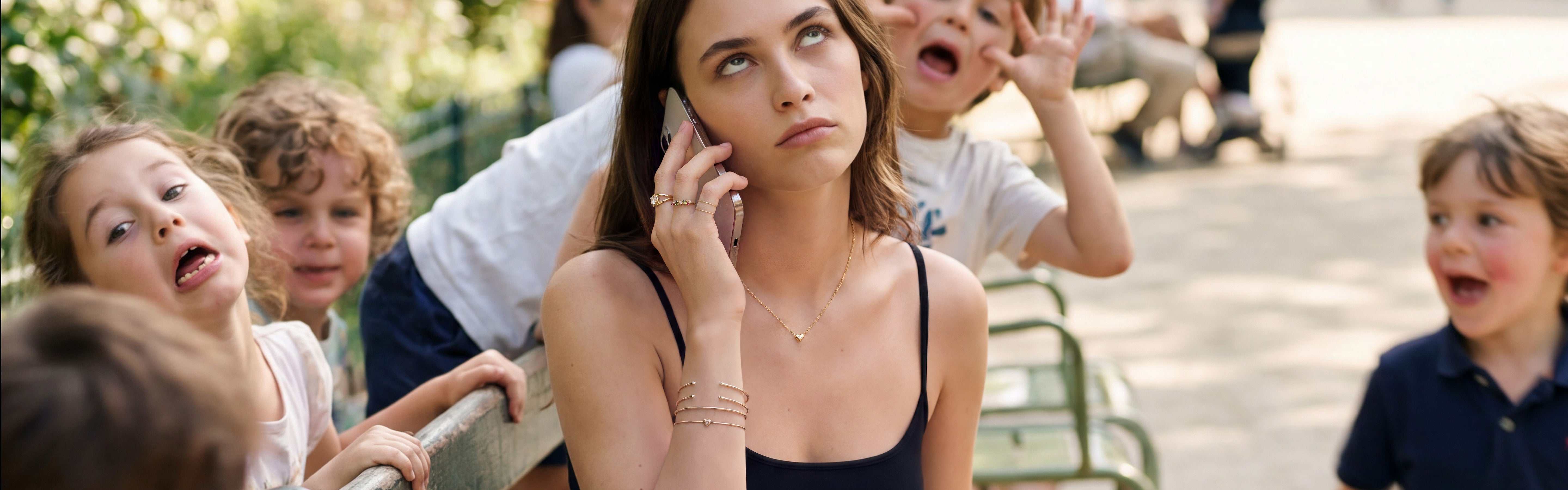 Une femme tente de travailler au parc à Paris, l'été. Elle est entourée d'enfants qui jouent et porte des bijoux Monsieur Paris